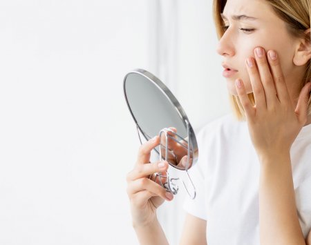 A woman examining her acne-prone skin in the mirror, pleased with the improvement by following clear skin steps.