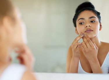 Mujer mirándose al espejo con problemas de acné en la piel 